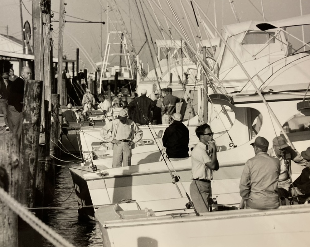 A photo from the 1950s showing sport fishing students standing in several boats, which sit in the harbor