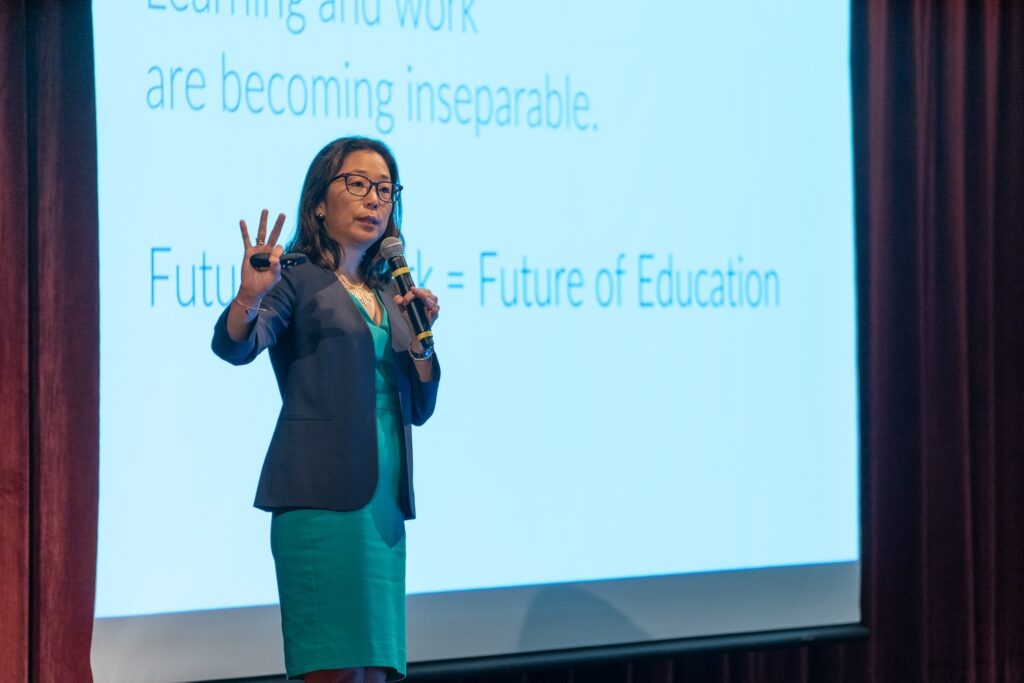 Michelle Weise speaking in front of a large projector screen that mentions the future of education