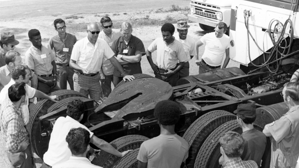 A photo of the Truck Driving School from the 1960s, showing attendees gathered around the chassis of a truck