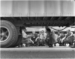 A photo of the Truck Driving School from the 1960s, showing attendees gathered around the chassis of a truck