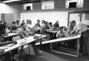 Attendees sit in a classroom observe an instructor demonstrating truck safety using a model truck