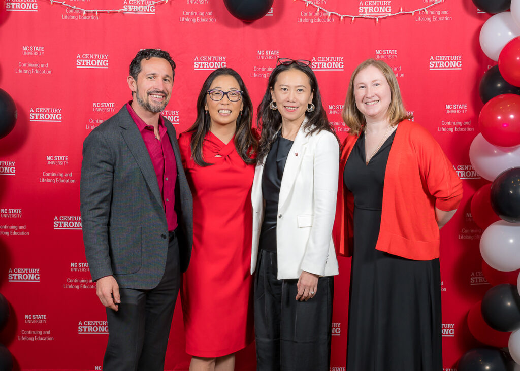 Scott O'Leary, Michelle Weise, Helen Chen, and Eliza Kiser pose in front of the 100-year celebration backdrop.