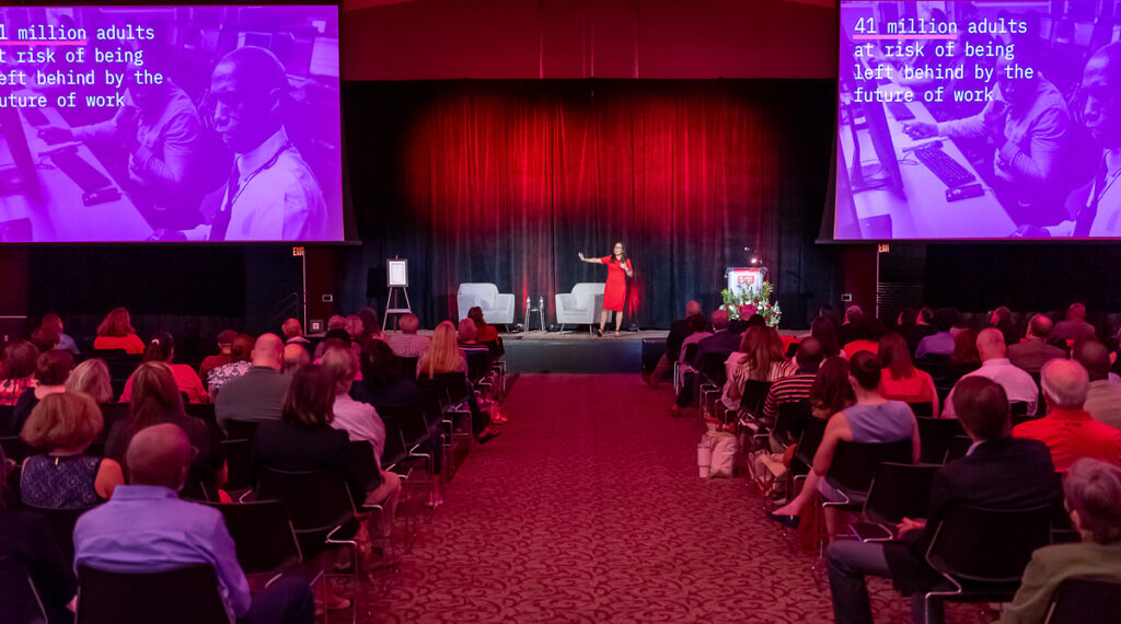 Michelle Weise on stage with the audience listening. The screen says 41 million adults at risk of being left behind by the future of work.
