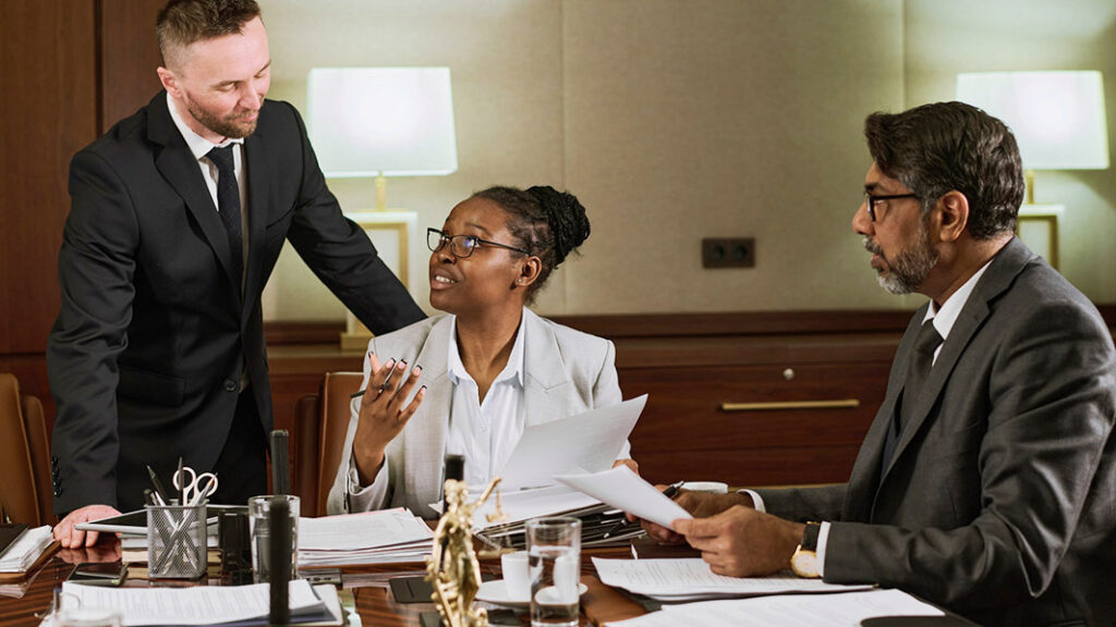 Young confident African American paralegal looking at one of two male colleagues during discussion of main points of authentication of document needing notarization.