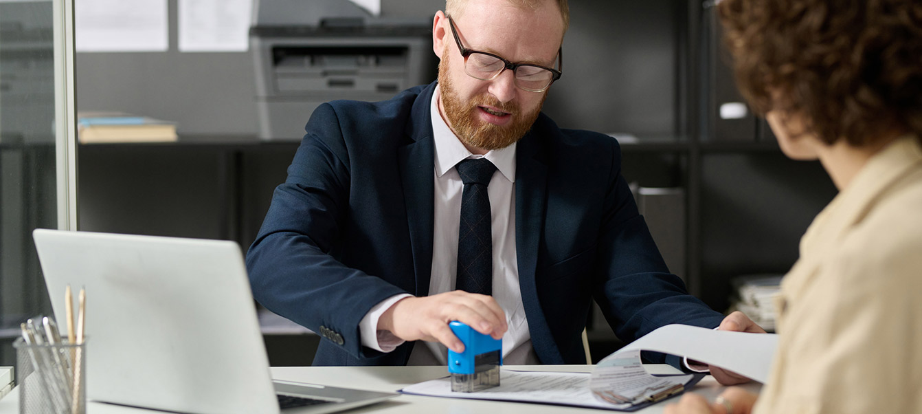 Bearded man notary stamping document while working with female client at office